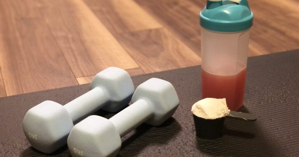 ダンベルとシェイカーを並べたプロテイン補給のイメージ